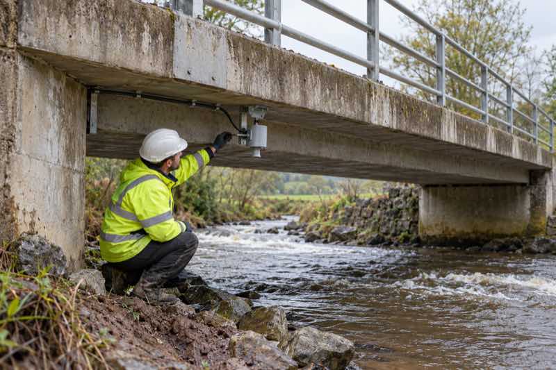 Technician inspecting a non-contact water level sensor beneath a bridge