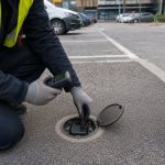 Technician servicing a smart parking sensor battery in an urban parking bay.