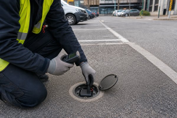 Technician servicing a smart parking sensor battery in an urban parking bay.