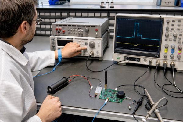 Engineer measuring LoRaWAN and NB-IoT current pulses from a smart parking sensor battery.